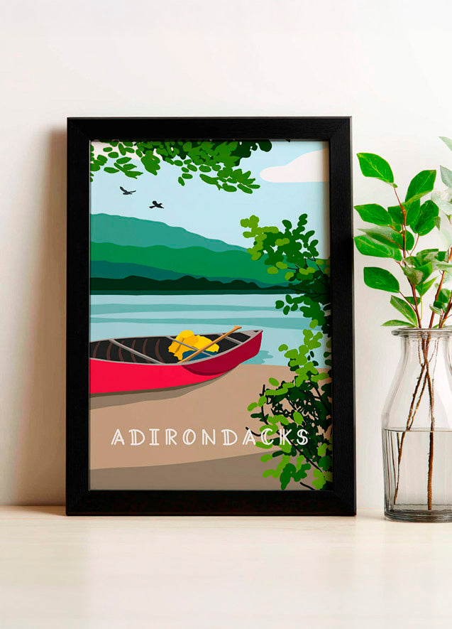 Framed artwork of a lake scene with a red canoe and 'Adirondacks' text, placed on a white surface.