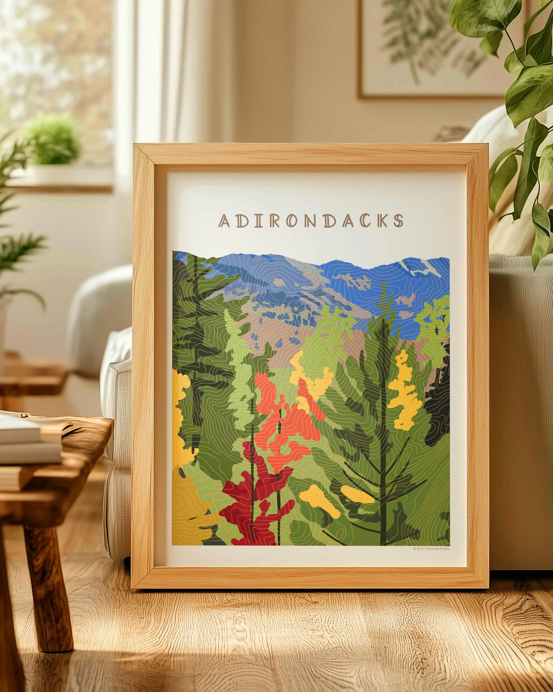 Framed illustration  of a fall foliage scene in the Adirondacks with topographic contour lines overlaying the image. Words Adirondacks at the top. 