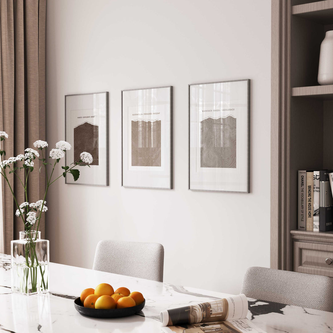 Mockup of framed set of three topographic map art prints of Mount Marcy, Skylight &amp; Gray, Algonquin, Iroquois &amp; Wright Peaks, Haystack, Basin and Saddleback peaks in brown line patterns on a white background in a dining room