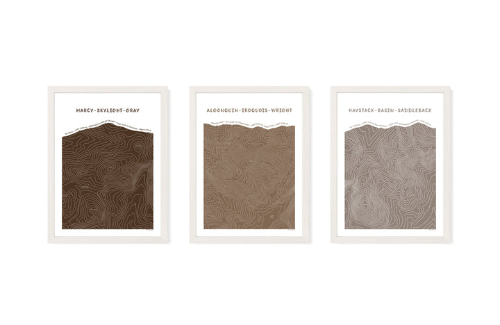 White framed set of three topographic map art prints of Mount Marcy, Skylight &amp; Gray, Algonquin, Iroquois &amp; Wright Peaks, Haystack, Basin and Saddleback peaks in brown line patterns on a white background